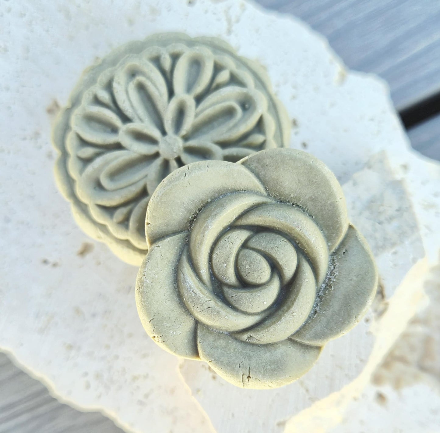 two decorative solid shampoo bars with rose and botanical shapes displayed on stone surface.