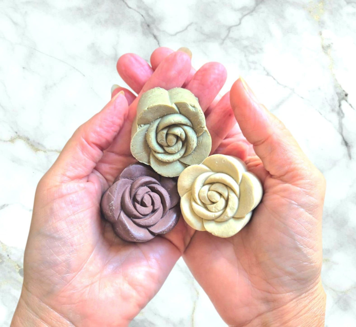 Three solid clay shampoo bars with rose shapes held in hands against a marble background