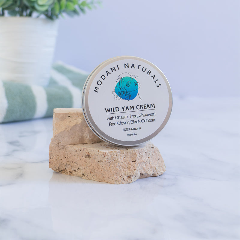 A tin of Wild Yam Cream with label displayed on stone pedestal on light background with a plant and bath towel.