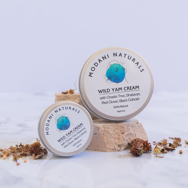 2 size versions of modani naturals wild yam cream displayed on stone pedestals on white background with botanicals.