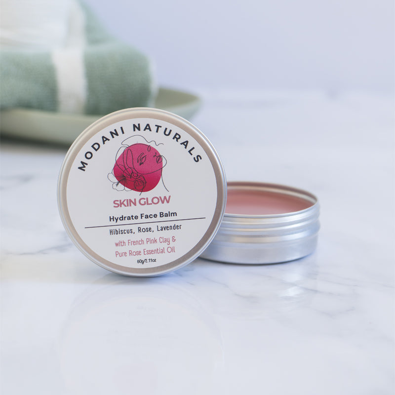 Open tin of Modani Naturals Skin Glow Hydrate Face Balm with Hibiscus, Rose, Lavender showing contents and colour of product on marble surface.