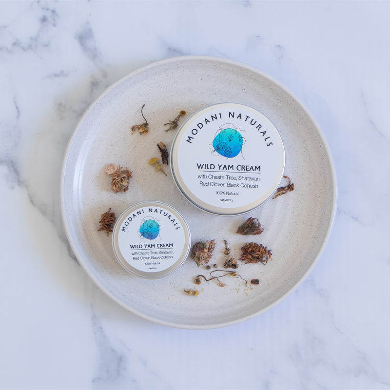 modani naturals wild yam cream showing 2 tins with scattered botanicals on ceramic dish. Small and large.