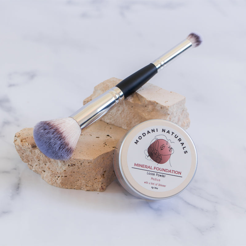 modani naturals makeup brush and mineral foundation powder displayed on stone pedestal with marble background.