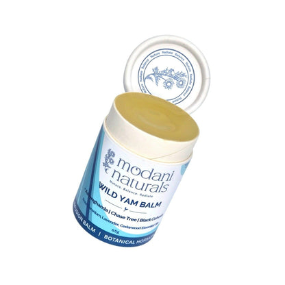 An open cardboard push up tube of Modani Naturals Wild Yam Balm with its lid propped behind it, showing the pale yellow balm inside and a blue and white label on a plain white background.