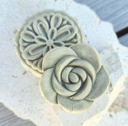 two decorative solid shampoo bars with rose and botanical shapes displayed on stone surface. 