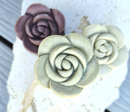 3 rose shaped solid shampoo bars in 3 colours displayed on stone surface. 