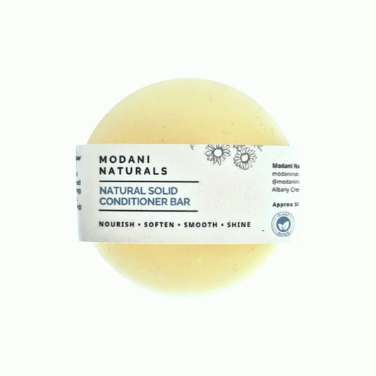 A round pale yellow Modani Naturals solid conditioner bar wrapped in a white paper label, shown against a plain white background.